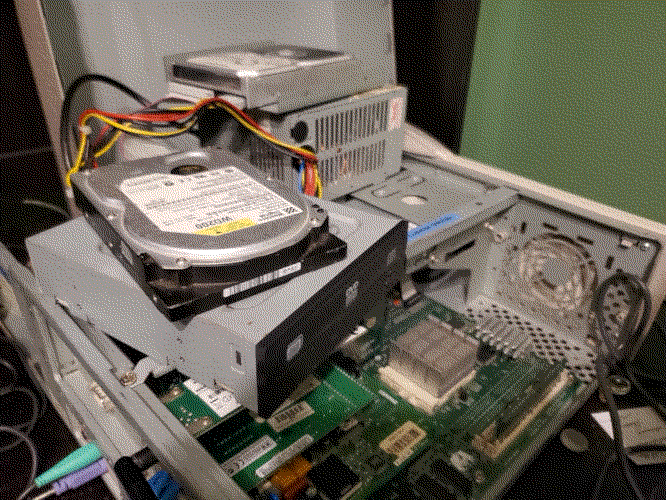 Hard disk drive precariously perched atop a DVD-ROM drive which in turn is precariously perched on top of a few bars going across an open computer chassis